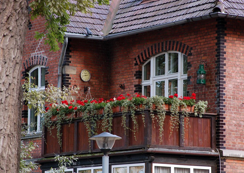 Ten mieszczański balkon ozdobiony kwiatami wpasowałby się tak samo dobrze w polskie, jak i angielskie podwórze.